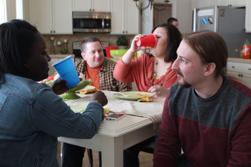 Groups of people around kitchen table, eating and drinking