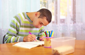 Young man writing at a desk with coloured pens