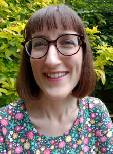 Woman with fringe and bobbed brown hair wearing glasses and smiling.