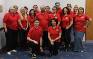 Group photo of the Learning Disability Wales team. Everyone is wearing red polo shirts, smiling and looking at the camera