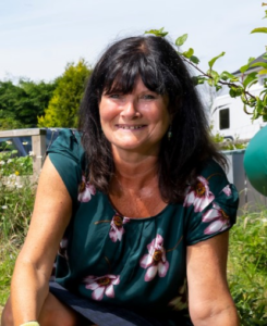 Rhian has dark long hair and is sat in her garden on a sunny day.