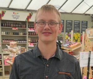 James has short blond hair and is wearing glasses and is in a shop.