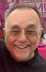 John has cropped hair, is wearing glasses and smiling