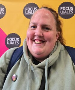 Victoria has brunette hair and is wearing a grey hoody with Gig Buddies Cymru badge