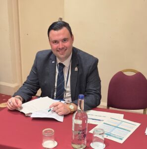 young man in a suit at a table smiling and reading some documents
