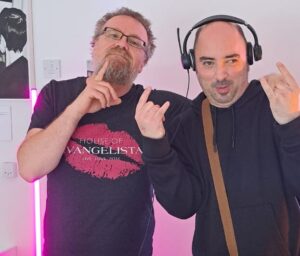 Kai has glasses and a beard and is posing with his friend who is wearing DJ headphones