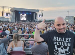 young man at a huge outdoor gig with the crowd and the stage behind him