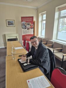 A man wearing a suit and glasses sitting at a table smiling for the camera