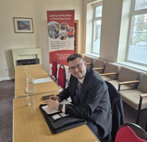 A man wearing a suit and glasses sitting at a table smiling for the camera