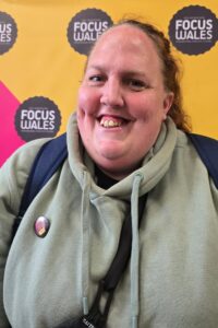 A person smiling at the camera. Hair pulled back, wearing a grey jacket