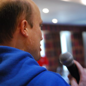 Balding man in blue hoodie speaking into a microphone