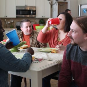 Groups of people around kitchen table, eating and drinking