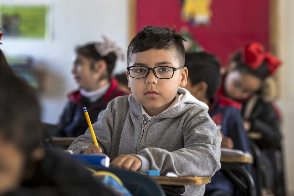 Child sitting at school desk with pencil in his hand