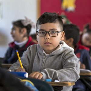Child sitting at school desk with pencil in his hand