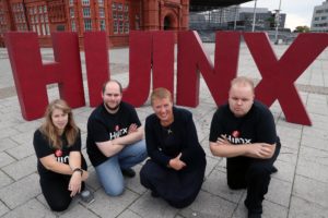 Actors from Hijinx Theatre kneeling infront of large red letters that spell out Hijinx