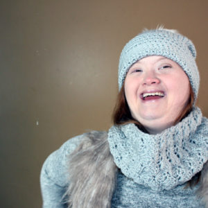A woman laughing, wearing hat and scarf.  She looks confident.
