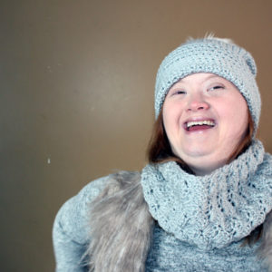 A woman laughing, wearing hat and scarf. She looks confident.