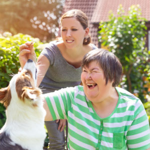 2 wome, one of whom has down's syndrome, playing with a dog in a garden