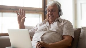 An older man is sitting on a sofa using a tablet to have a video chat