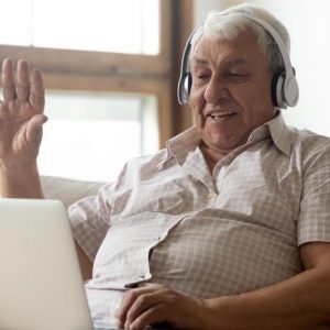 An older man is sitting on a sofa using a tablet to have a video chat