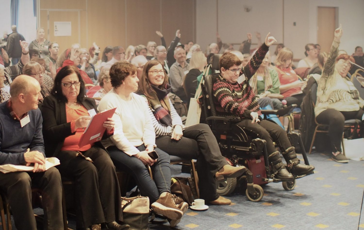 Audience at a Learning Disability Wales conference, some are raising their hands to ask a question