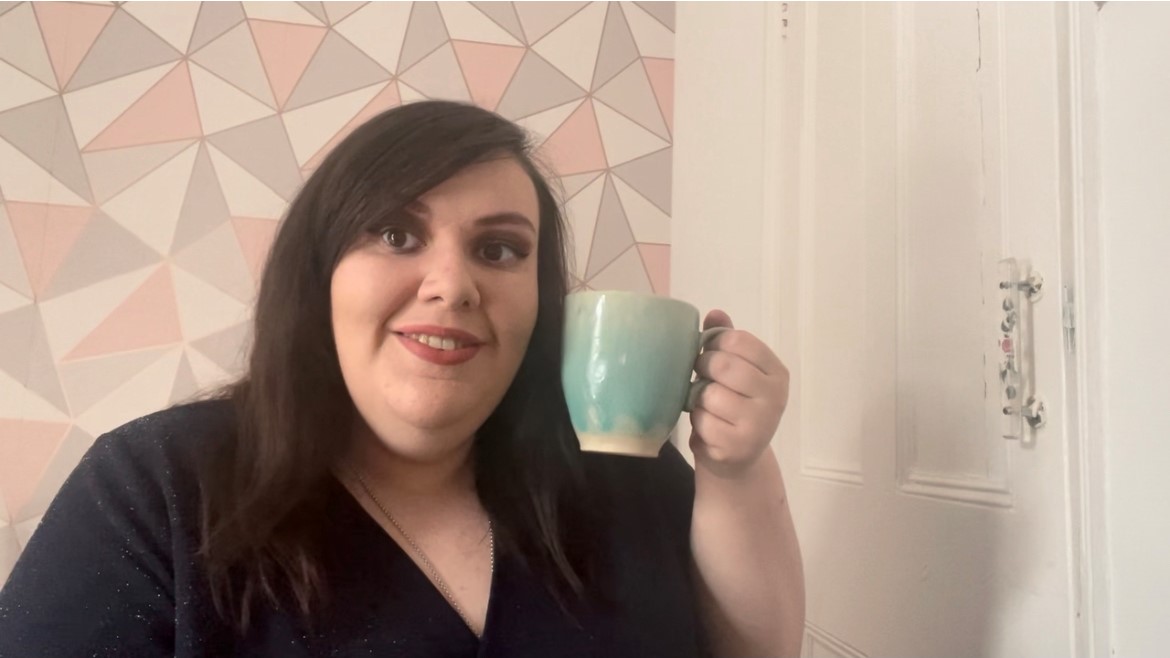 Woman with long brunette hair holding up a mug and smiling