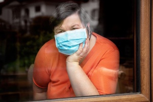 woman with down syndrome and wearing a mask looking out of a window unhappy