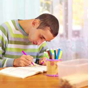 Young man writing at a desk with coloured pens